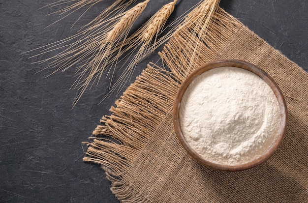 Wheat flour and dry branch on a dark background Organic baking ingredients Concept of homemade and healthy food