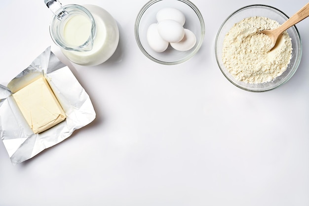 Wheat flour in the glass bowl cream in a glass jar butter chicken eggs ingredients for the dough top view