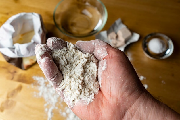 手に小麦粉を持って背景のテーブルの上にパンを作る材料を置く