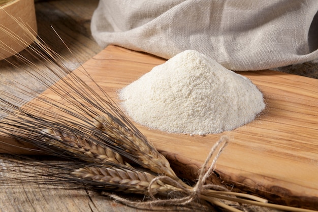 Wheat flour on a wooden cutboard and spikelets on a wooden table, close up