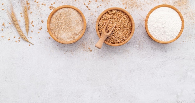 Wheat grains brown wheat flour and white wheat flour in wooden bowl set up on white concrete background