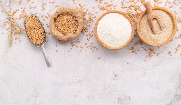 Grani di frumento farina di frumento marrone e farina di frumento bianca in una ciotola di legno allestita su fondo di cemento bianco