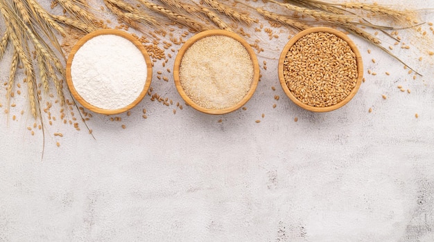 Grani di frumento farina di frumento marrone e farina di frumento bianca in una ciotola di legno allestita su fondo di cemento bianco