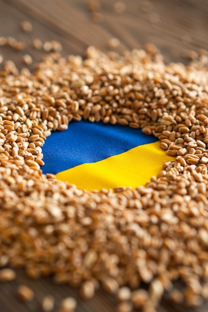 Wheat grains with yellow and blue ukrainian flag on wooden background