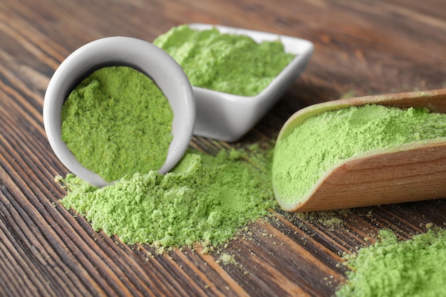 Wheat grass powder in kitchenware on wooden background