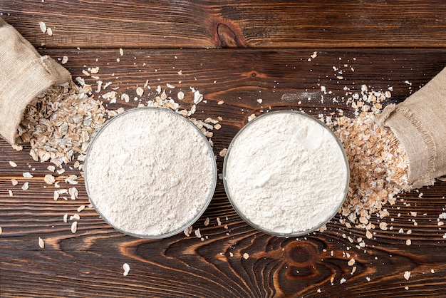 Wheat and rye flakes and flour on dark wood.