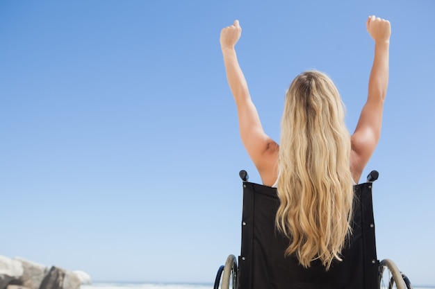 Photo wheelchair bound blonde sitting on the beach with arms up