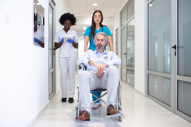 Пациент в инвалидной коляске с профессиональным афроамериканским врачом и медсестрой в коридоре реабилитационного центра больницы