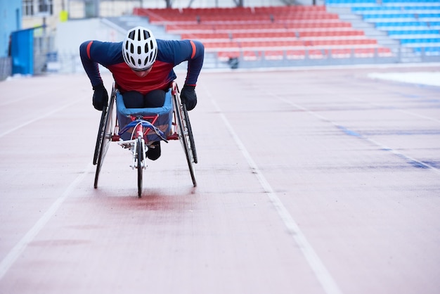 Foto corsa in carrozzina. sportivo portatore di handicap nel casco che copre la distanza in sedia a tre ruote specializzata su pista all'aperto