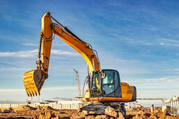 A wheeled excavator in a trench digs the ground An excavator with a highly raised bucket against a cloudy sky Earthworks at the construction site