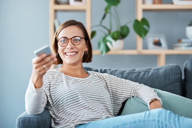 When that good ol television show comes on Cropped shot of a happy young woman using the remote control on the sofa at home