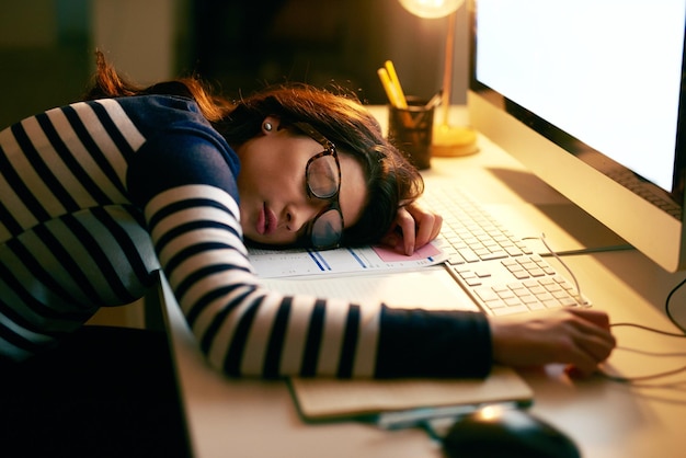 When you just cant keep your eyes open any longer Shot of a young businesswoman sleeping on her desk while working late in an office