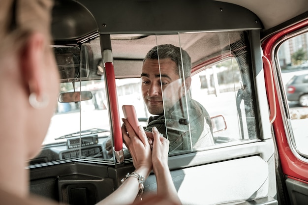 どこで運転するか。後部座席に座っている女性が、笑顔の車の運転手に地図を持ってスマートフォンを見せています。