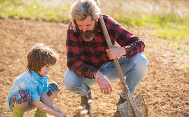 Photo where food comes from teaching son growing plants planting plants works in field father farmer instruct baby how to planting eco farming real skills dad with shovel and boy digging soil