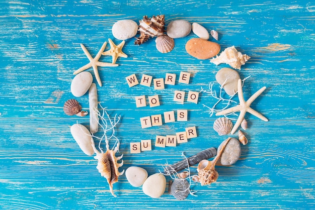 where to go this summer text in circle of shells on blue wooden background overhead view