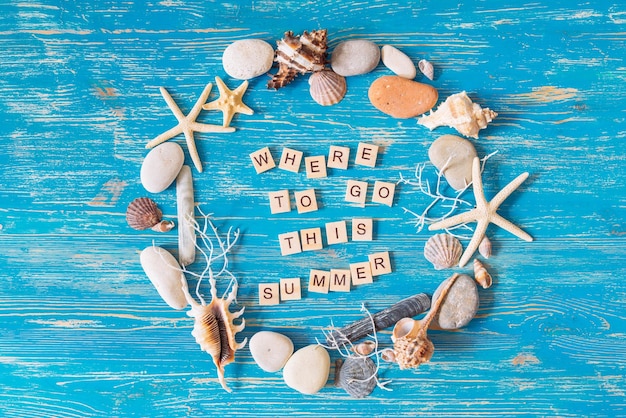 Photo where to go this summer text in circle of shells on blue wooden background overhead view