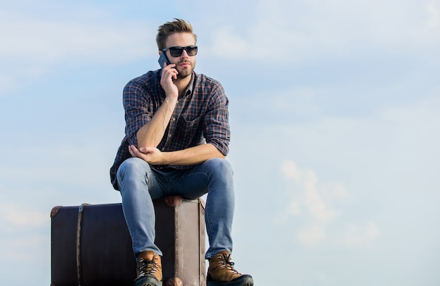 Where is my taxi. sexy man sky background speak on phone. male fashion style. looking so trendy. businessman in glasses. business trip. macho man tourist relax tour bag. traveler wait for taxi. Move.