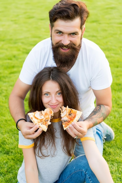 Qual è il tuo preferito. fast food. uomo barbuto che alimenta la pizza al formaggio della donna. le coppie innamorate che frequentano all'aperto mangiano la pizza. studenti affamati che condividono il cibo. coppia mangiare pizza rilassante sul prato. weekend in famiglia.