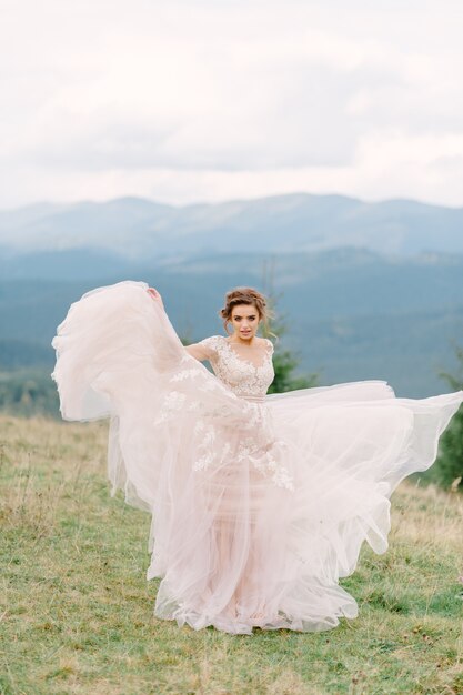 Whirling bride holding veil skirt of wedding dress at pine forest