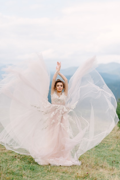 Whirling bride holding veil skirt of wedding dress at pine forest