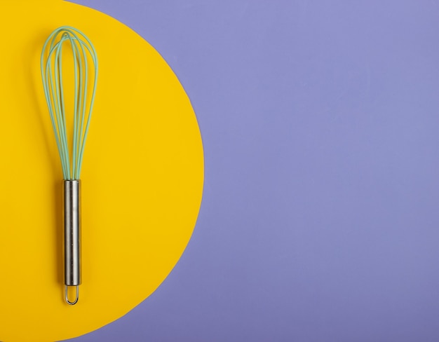 Whisk on blue with yellow circle.