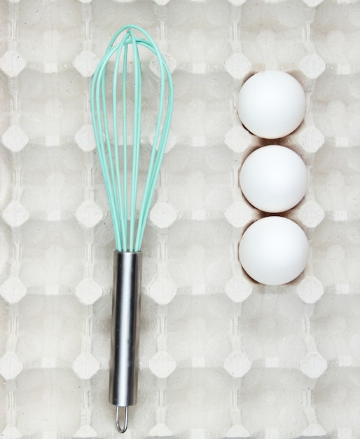 Whisk and eggs in tray. Top view, closeup