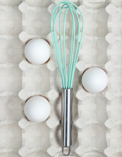 Whisk and eggs in tray. Top view, closeup