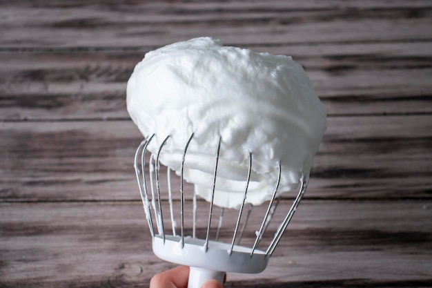 Whisk with whipped cream or whipped egg whites on a dark brown wooden background