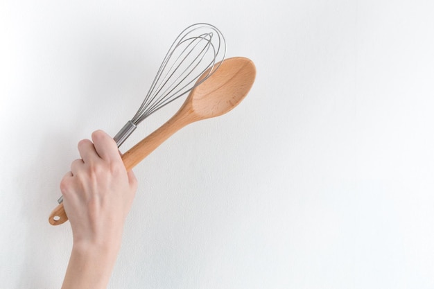 Whisk and a wooden spoon in a female hand on a white background Place for text or information