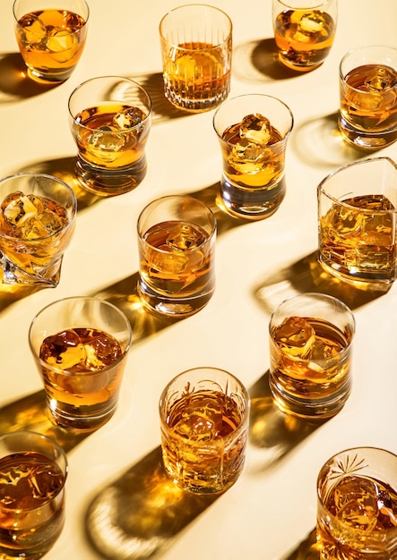 Photo whiskey and bourbon in luxury glasses with ice cubes on golden background