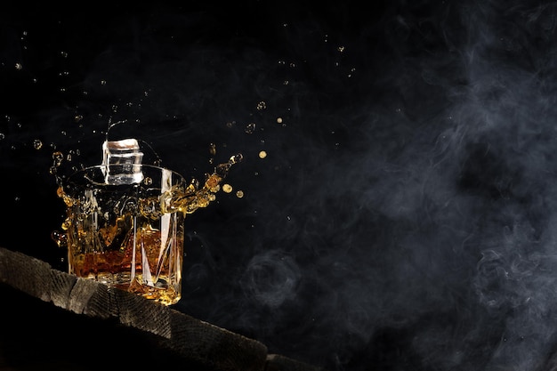 Виски в стакане на черном фоне на деревянном столе.