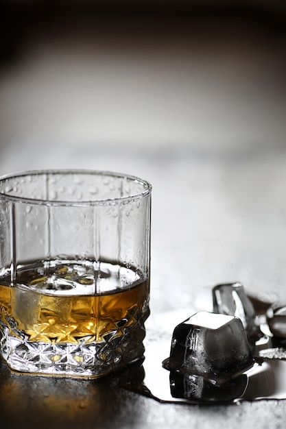 Whiskey in a glass and pieces of ice on a wooden table