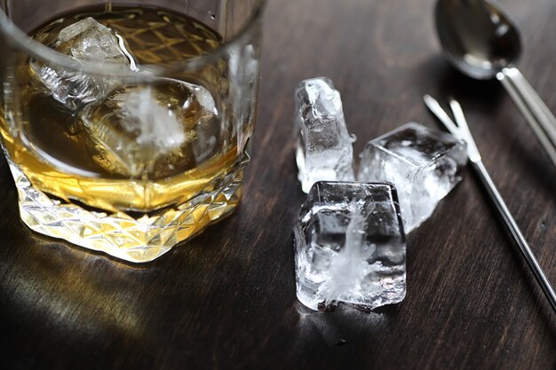 Whisky in un bicchiere e pezzi di ghiaccio su un tavolo di legno