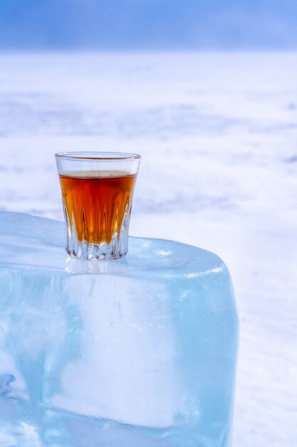 Whiskey in a glass stands on an ice block Orange alcoholic drink in a glass