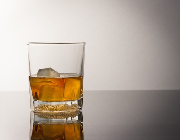 whiskey glass with ice cubes and reflection drink alcohol on grey 