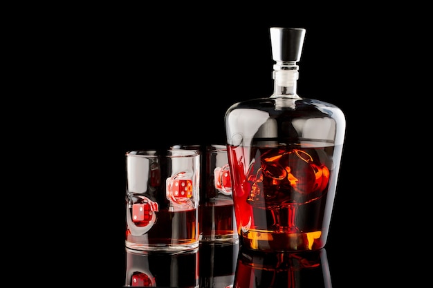 Whiskey glasses with rum or whiskey with red dices and decanter with scull on dark glass background