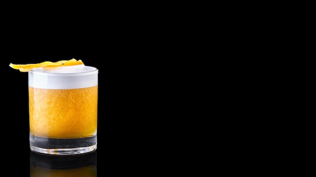 Whiskey sour cocktail served on the rocks isolated on a black background garnished with an orange slice