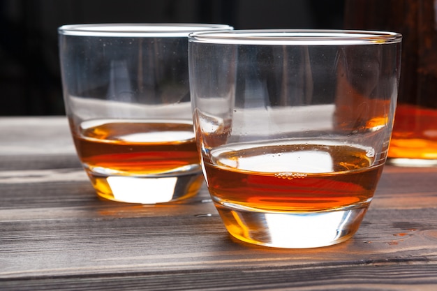 Whiskey with ice cubes on wooden table