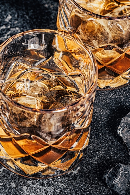 Foto whisky con ghiaccio su uno sfondo scuro di pietra.