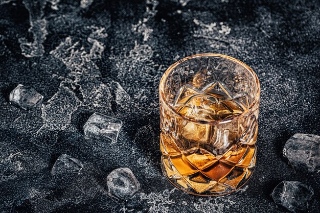 Photo whiskey with ice on a stone dark background.