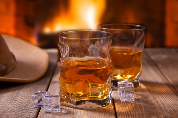 Whiskey with ice on a wooden table with fireplace and cowboy hats 