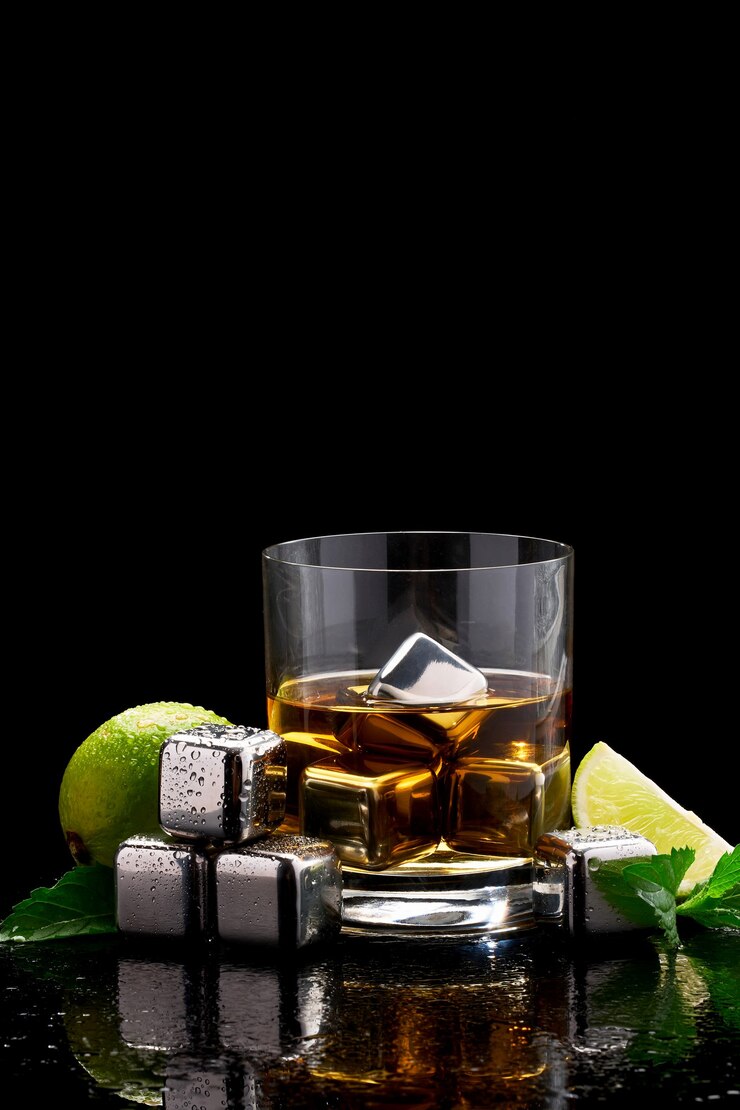 Whiskey with steel cooling cubes on glass on dark surface