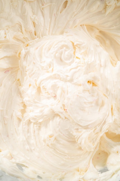 Photo whisking buttercream frosting in a glass mixing bowl with an electric hand mixer to prepare the peppermint buttercream frosting.