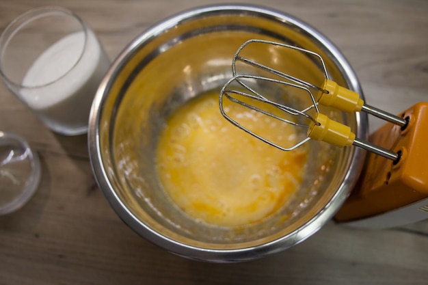 Photo whisks of electric mixer in front of sugar and eggs in a bowl