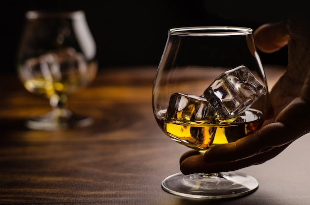 Whisky / cognacglas met ijs in een hand op hout