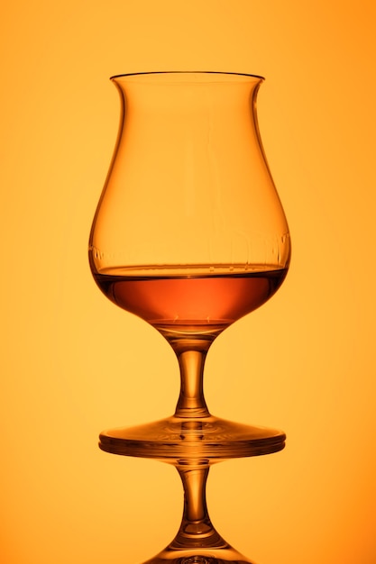 Foto whisky in un bicchiere a sfondo arancione