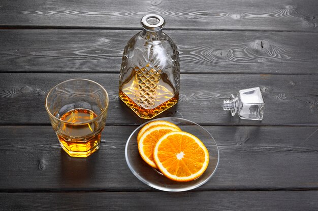 Whisky glass with orange fruit cut on dark wooden 