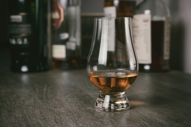 Whisky glass with single malt scotch on wooden table and scotch bottles