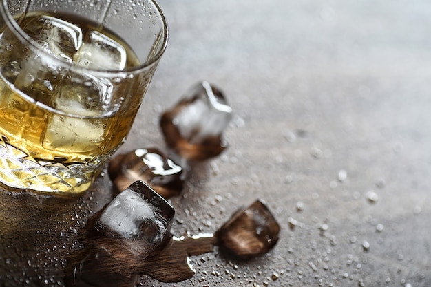 Whisky in een glas en stukjes ijs op een houten tafel