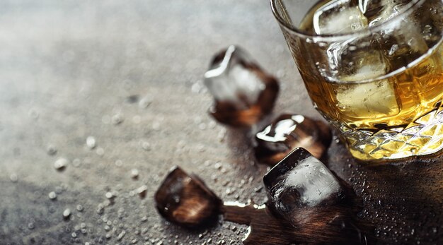 Whisky met ijs met een glas. Blokjes ijs op een houten tafel en een glas met gekoelde sterke alcohol. Tafel met Amerikaanse whisky, bourbon en kaarten.